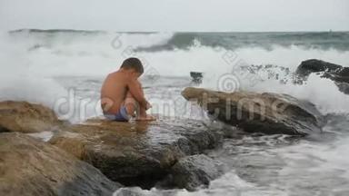 孩子在海边冲浪。 男孩坐在一块大石头上，享受<strong>海浪</strong>的<strong>声音</strong>。